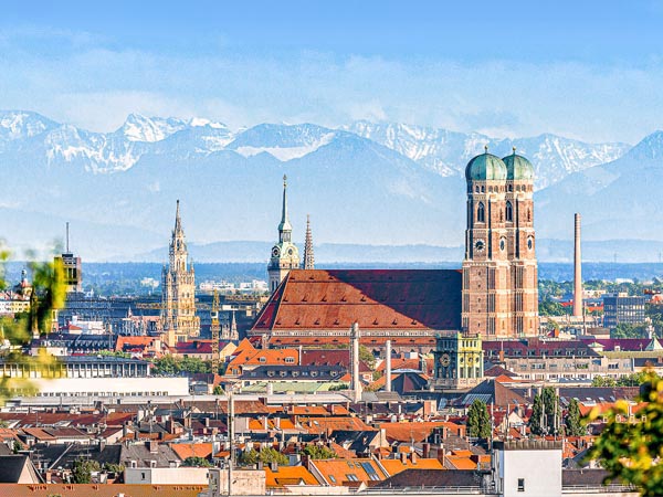 Blick über München mit Frauenkirche vor Alpenpanorama - die perfekte Kulisse für Ferien in Bayern 2024.