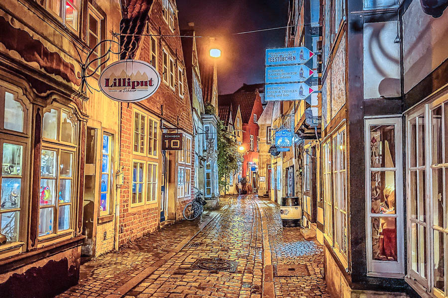 Nächtlich beleuchtete romantische Gasse im Schnoorviertel mit Geschäften und Boutiquen - eine faszinierende Kulisse für Ferien in Bremen